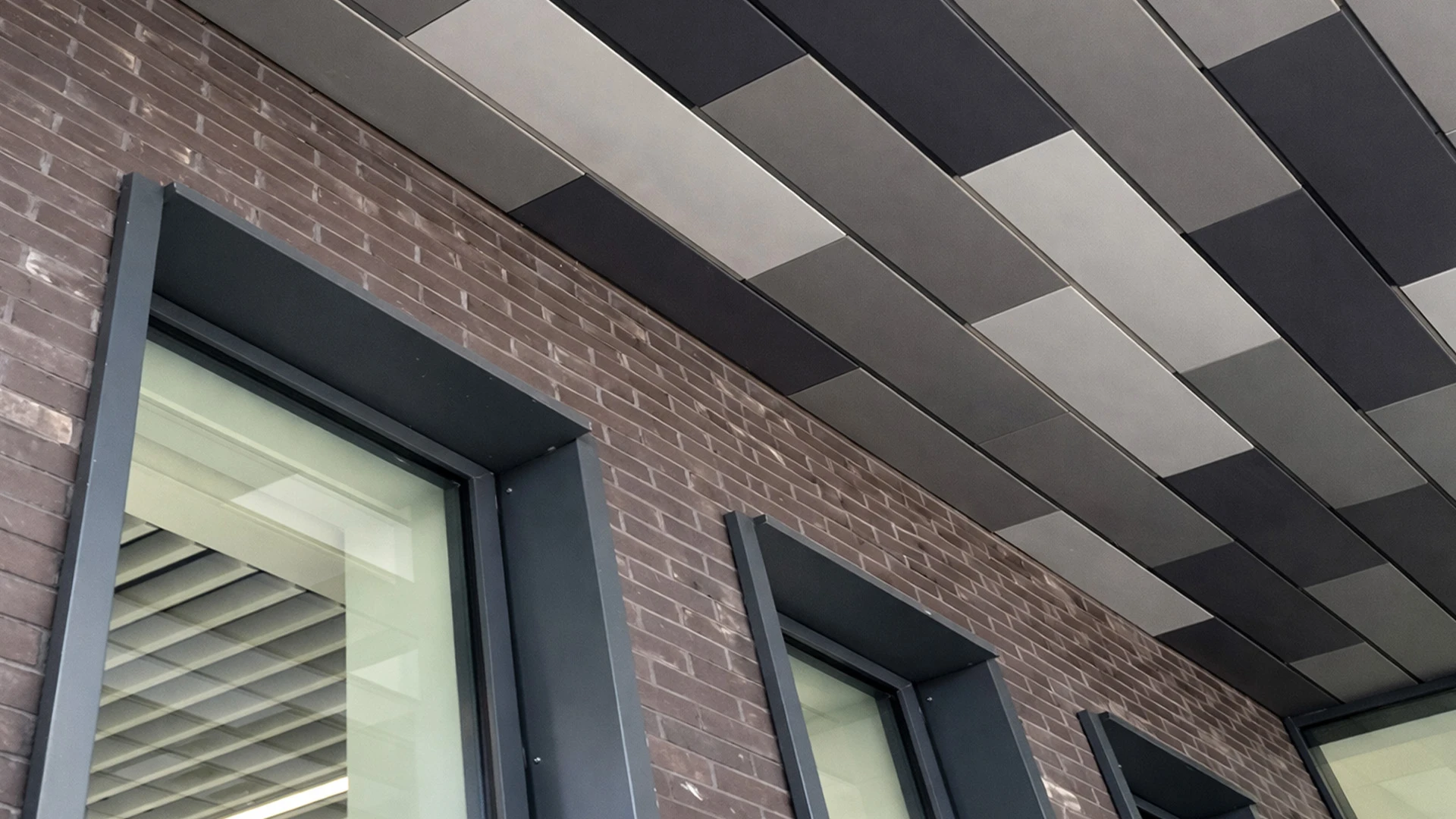 Detail view of a brick building façade with recessed windows and metal soffit panels forming a patterned overhang