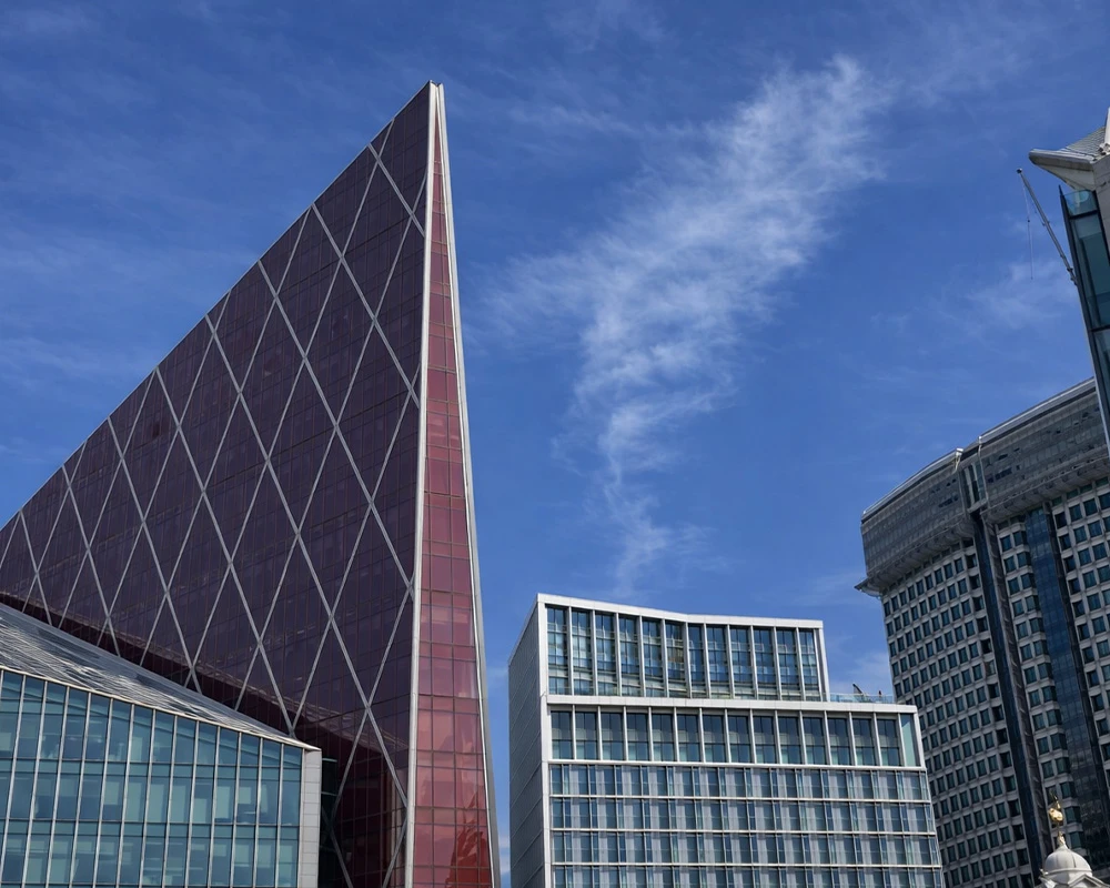 Contemporary city buildings with glass and metal façades, featuring distinctive angular architecture against a clear blue sky
