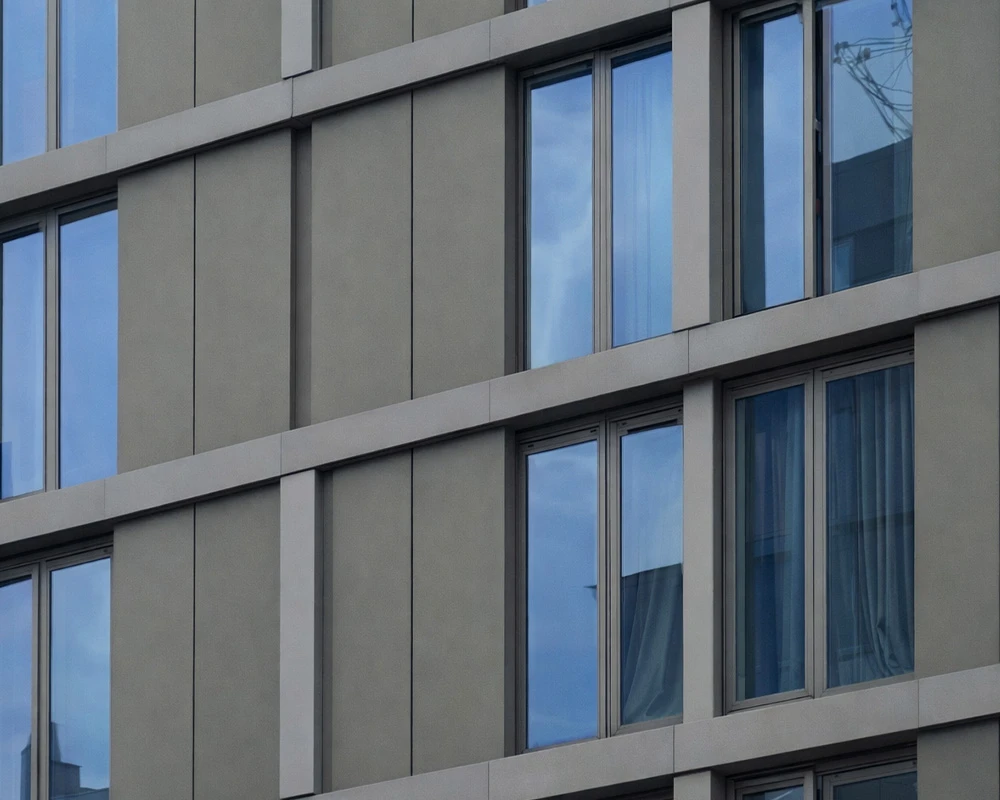 Modern building façade with vertical cladding panels and recessed glazed windows reflecting the surrounding urban environment