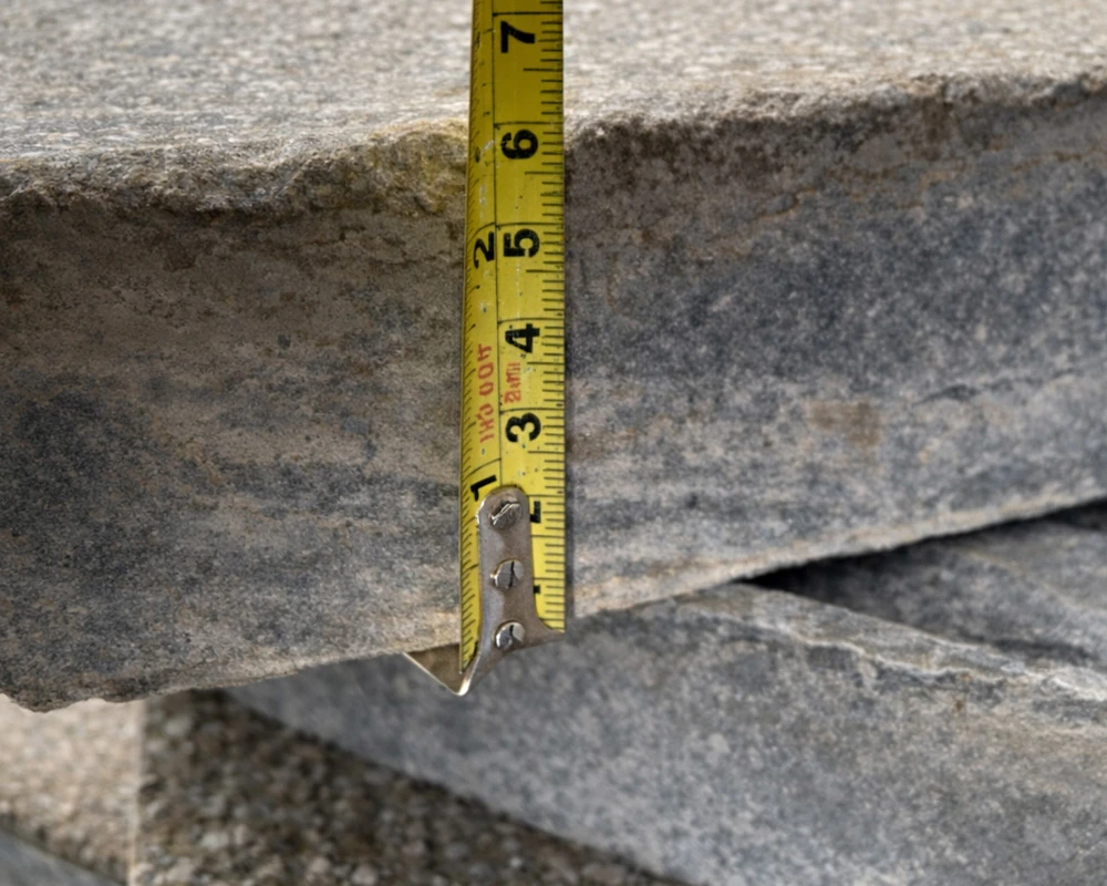 Close-up of a tape measure showing the thickness of stone cladding panels during building inspection or assessment